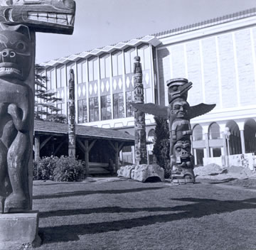 View of Totem Poles in Thunderbird Park with the Museum in the Background.