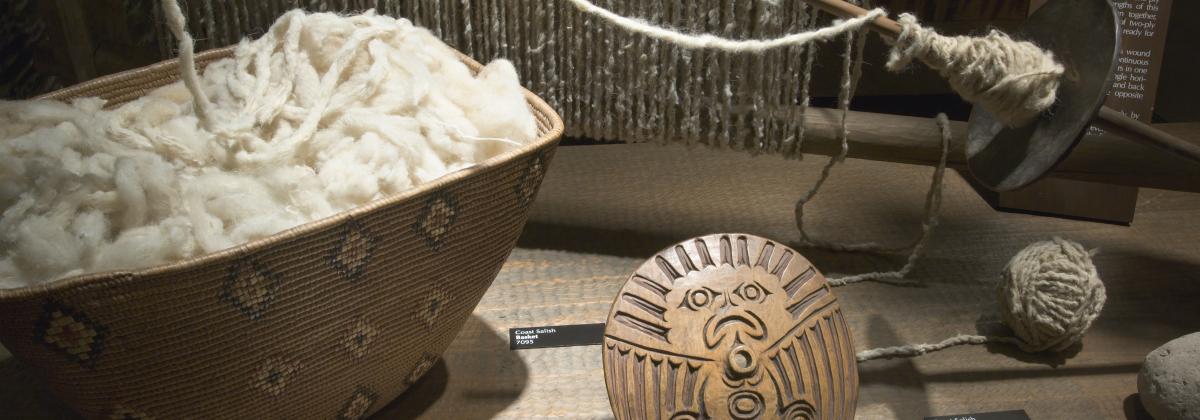 A basket of wool, next to and attached to an Indigenous spindle whorl